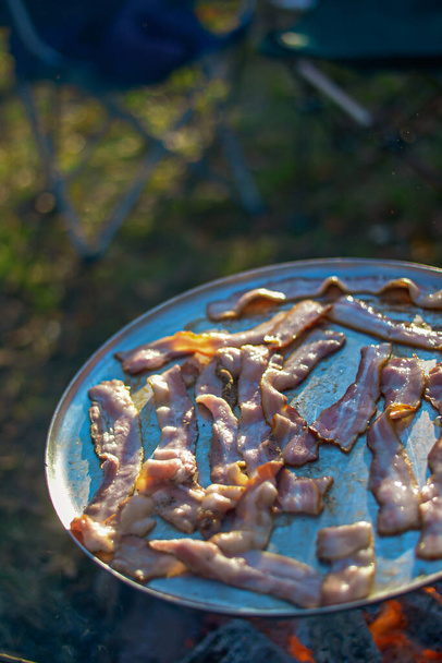 Cucinare pancetta su un falò ricreativo al di fuori
 - Foto, immagini