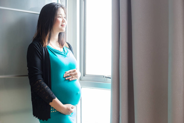 Όμορφη ευτυχισμένη ασιατική έγκυες γυναίκες στέκεται στο δωμάτιο από το παράθυρο, Ελπίδα έννοια - Φωτογραφία, εικόνα