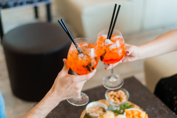 Women holding glasses of aperol spritz cocktails at cafe. Traditional Spritz aperitif. - 写真・画像