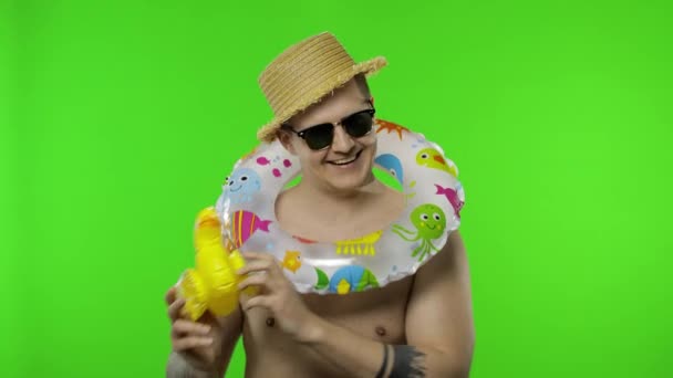 Mladý muž bez košile turista s plaveckým prstenem na ramenou hraje s kachní hračkou - Záběry, video