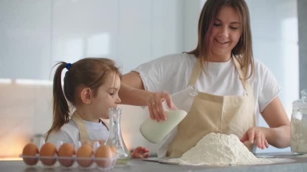 Doma, v kuchyni, matka a dcera rozbijí vejce a přidají mléko do mouky na dort. Domácí vaření a vaření těstoviny a pizza - Záběry, video