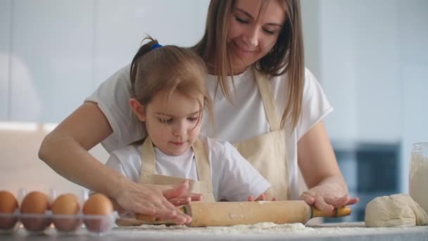 Hija y madre en casa en la cocina en delantales verter el despliegue de harina con un rodillo y esculpir la masa con las manos juntas. Pase tiempo con los niños y transmita la experiencia
. - Metraje, vídeo
