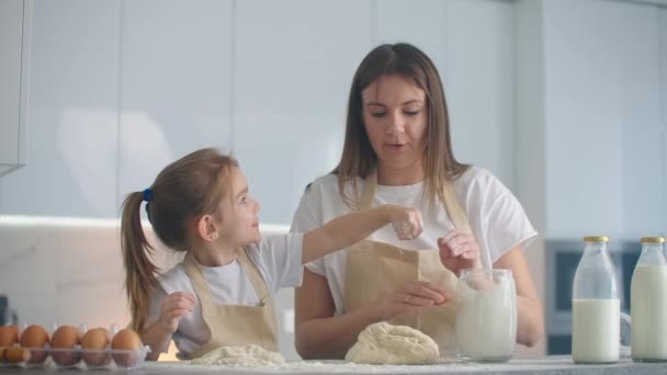 Fille et mère à la maison dans la cuisine dans des tabliers verser le rouleau de farine avec un rouleau à pâtisserie et sculpter la pâte avec leurs mains ensemble. Passez du temps avec les enfants et transmettez votre expérience
. - Séquence, vidéo