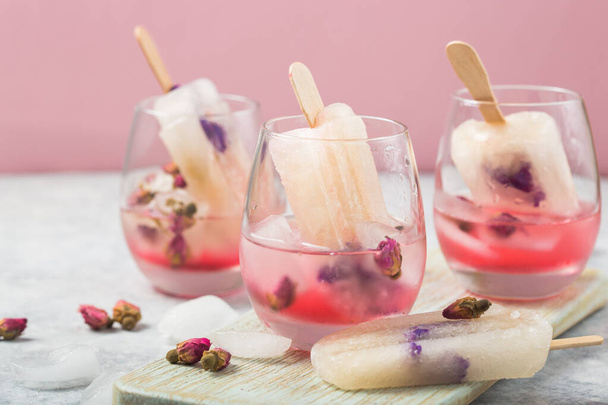 Kolorowe jedzenie. Szklanki koktajlowe różowego szampana różowego lub lemoniada z suchymi pączkami róż, lody - Zdjęcie, obraz