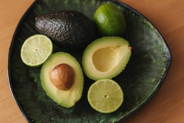 Авокадо і лайм половинки на зеленій пластині. Вегетаріанська концепція їжі. Краєвид - Фото, зображення