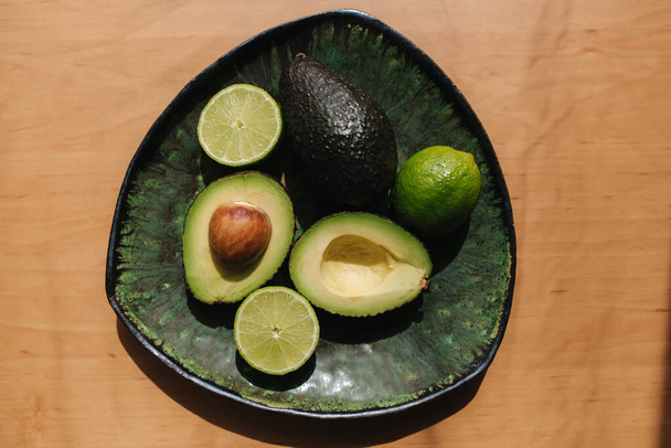 Avocado and lime halves on green plate. Vegetarian food concept. Top view - Photo, Image