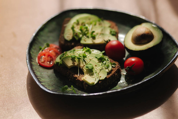Vegetarian breakfast at home. Sandwich with fresh sliced avocado above rye bread with cherry tomatoes on green plate - Fotografie, Obrázek
