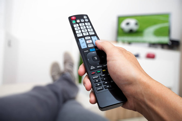 A ver televisão. Controle remoto na mão. Ver futebol na TV. Homem deitado no sofá assistindo TV
 - Foto, Imagem