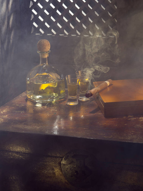 Крупный план бутылки текилы анехо и сигары на цветном фоне - Фото, изображение