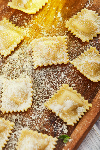 Tasty raw ravioli with flour, cherry tomatoes, sunflower oil and basil on a light wooden background. The process of making Italian ravioli. Flat lay. Close-up. - Foto, afbeelding