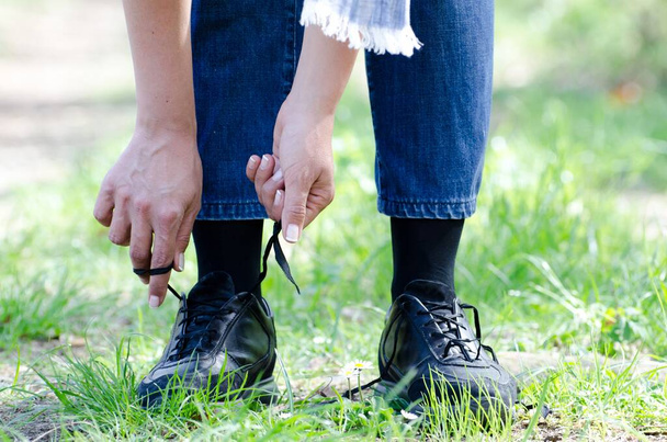 A closeup shot of a female tying her shoelaces on a path with grass - Photo, Image