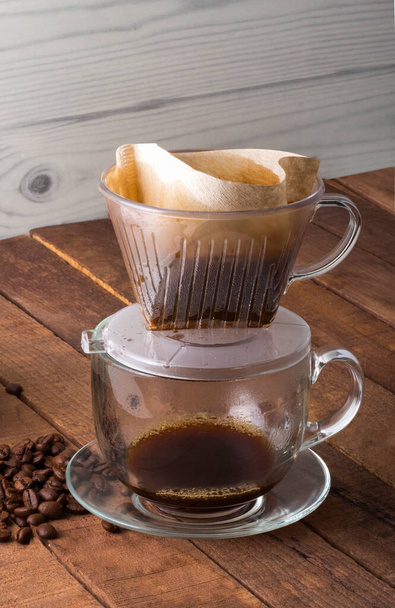 preparación alternativa de café en una taza a través de un filtro con granos de café sobre la mesa
. - Foto, Imagen