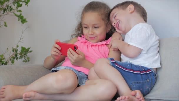 Happy children playing at home relaxing use a smartphone cuddling sit on sofa daughter and son,look at the screen of a cell phone, watch cartoons. - Metraje, vídeo