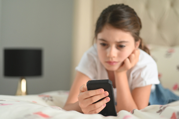 Sad girl (age 10) reading a bullying post on social media. Real people. Copy space - Foto, Imagem