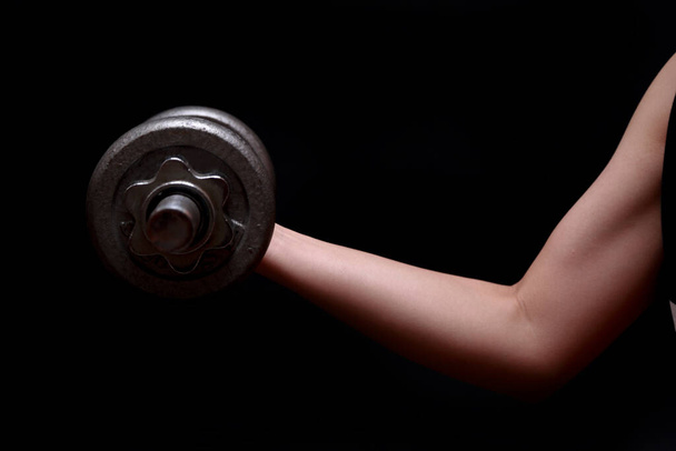 Closeup of  arm attractive athletic woman with dumbbell on dark background. - Photo, Image