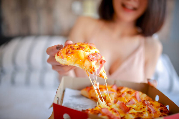 Retrato interior de una hermosa mujer feliz en su habitación, ella está en la mano sosteniendo una pizza estirándose y sonriendo
. - Foto, Imagen