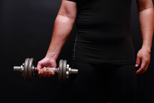 Closeup of  arm attractive athletic man with dumbbell on dark background. - Фото, зображення