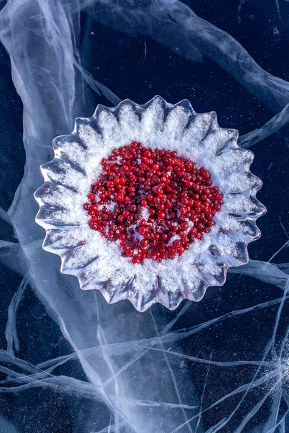 クランベリーの美しい氷の料理は、クラックとバイカル湖の氷の上に立っています。アイスカット皿の上に赤い果実。バイカル湖でのゲストを満たすためのロシアのシベリアの習慣。垂直. - 写真・画像