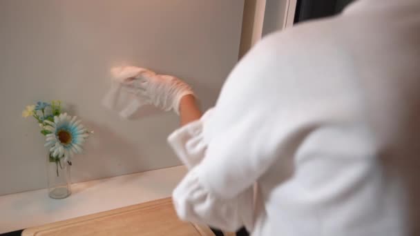 白い手袋の女性は、顔のマスクを着用し、噴霧し、拭くことによってキッチンの壁を消毒し、ウイルスが拡散し、汚染された表面、コロナウイルスcovid-19 、家庭用クリーナー、後ろからの眺めを防ぐ - 映像、動画