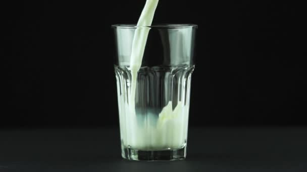 Melk gieten in geslepen glas close-up geïsoleerd op zwarte achtergrond Slow motion - Video