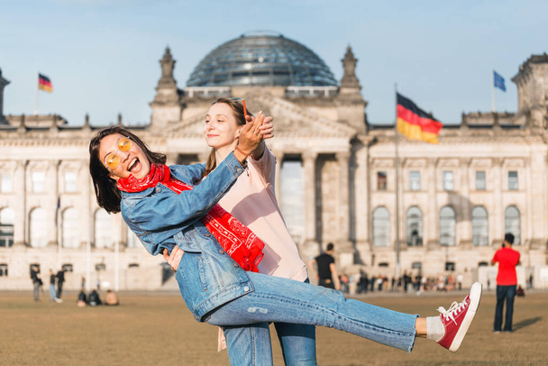 Duas amigas - estudantes ou turistas divertem-se e divertem-se no relvado perto do edifício Bundestag, em Berlim. Alemanha após a pandemia e o bloqueio de Covid-19
 - Foto, Imagem