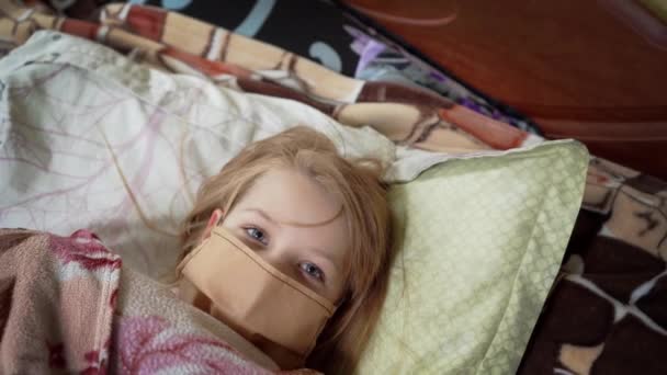 La petite fille est malade. Allongé sur un lit dans un masque médical, recouvert d'une couverture
. - Séquence, vidéo