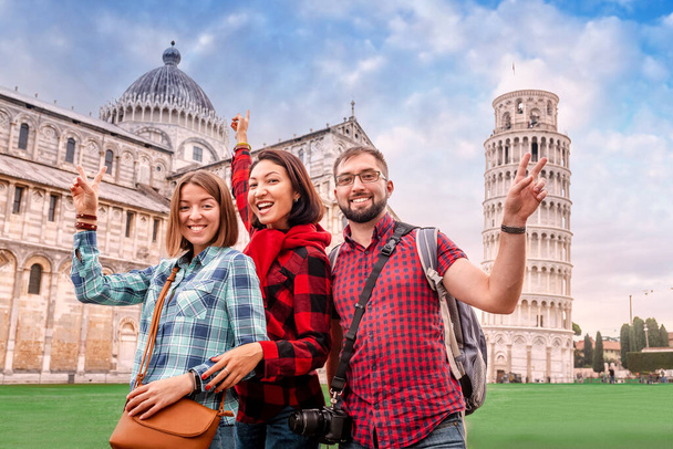 Zábavná a rozmanitá skupina mladých turistických přátel pózuje na pozadí slavné nakloněné věže v Pise. Cestovní ruch v Itálii po zrušení koncepce karantény a uzamčení - Fotografie, Obrázek