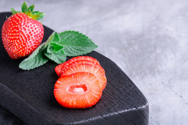 Fresh strawberry slices and mint on a cutting board in gray concrete background - Fotó, kép