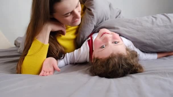 Loving happy young mother kissing cute little daughter lying on bed relish time together at home, expressing love, smiling mom and kid girl having fun playing, sincere warm relationships concept - Video