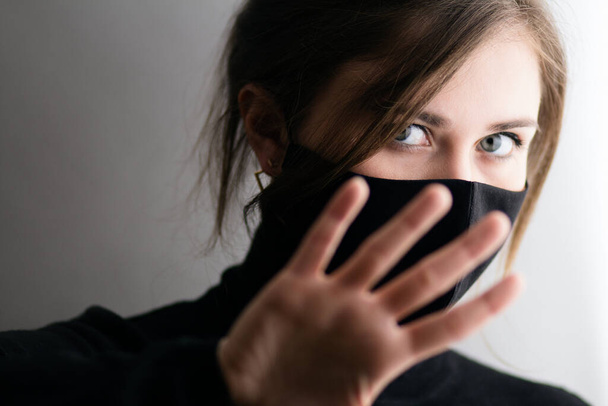 young woman in black mask defends herself from attention, girl palm covers her face, privacy concept - 写真・画像