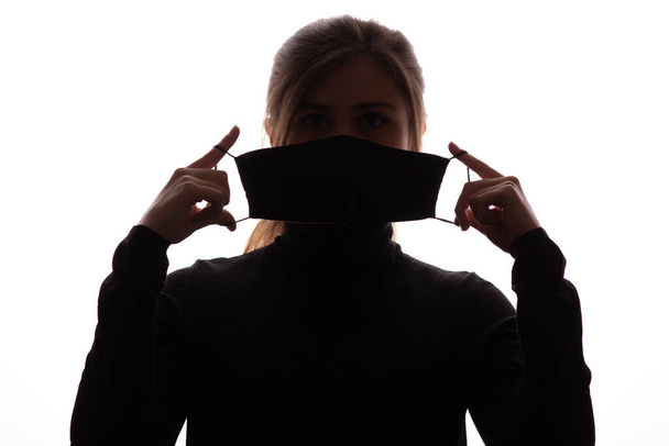 silhouette of young woman showing opened protective mask covering face on white background, quarantine measures and life saving concept - Zdjęcie, obraz