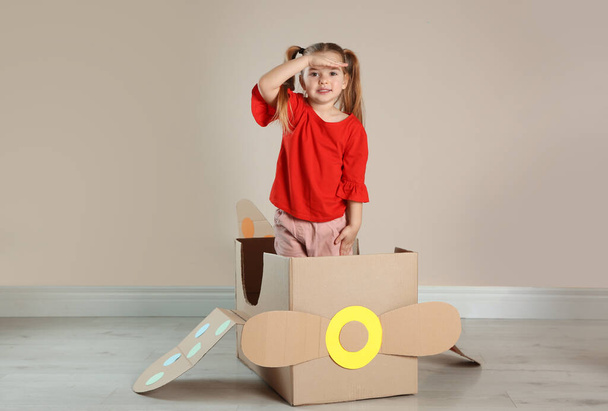 Cute little child playing with cardboard plane near beige wall - Zdjęcie, obraz