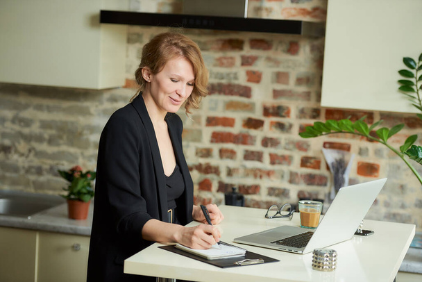 Une jeune femme travaille à distance sur un ordinateur portable dans sa cuisine. Une patronne est heureuse avec ses employés lors d'une vidéoconférence à la maison. Un enseignant écrit les réponses des étudiants lors d'une conférence en ligne
. - Photo, image