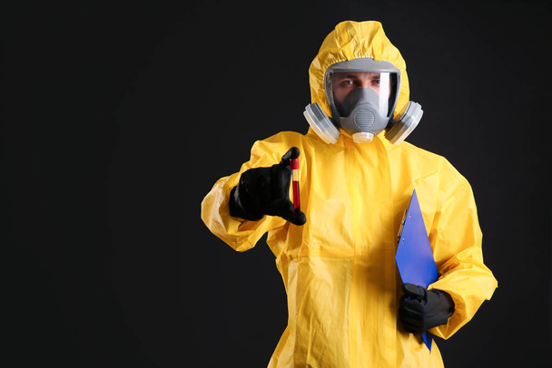 Man in chemical protective suit holding test tube of blood sample on black background, space for text. Virus research - Fotó, kép