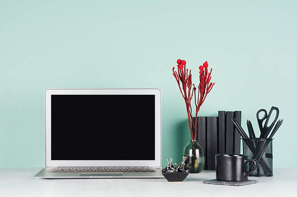 Spring office interior  - workplace with blank laptop display, black stationery, books, coffee cup, red decoration twig in light green mint menthe interior on white wood desk. - Фото, изображение