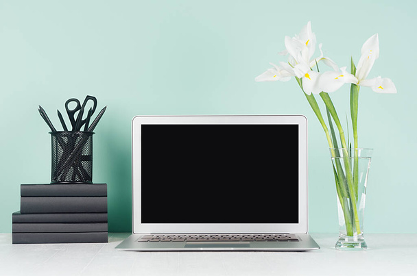 Fresh spring workplace for work and study with blank laptop display, black stationery, books and white bouquet in light green mint menthe interior on white wood desk. - Foto, Imagen