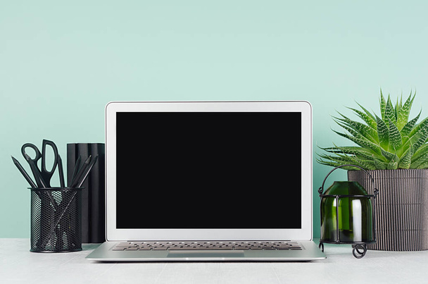 Simple minimalistic office interior with blank laptop monitor, black stationery, books, candlestick, aloe plant in elegant green mint menthe interior on white wood table. - Foto, Imagen