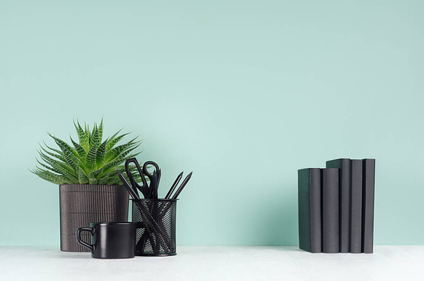 Spring interior - workplace with black stationery, books, green house plant, coffee cup, aloe plant in soft light green mint menthe color wall on white wood desk, copy space. - Photo, image