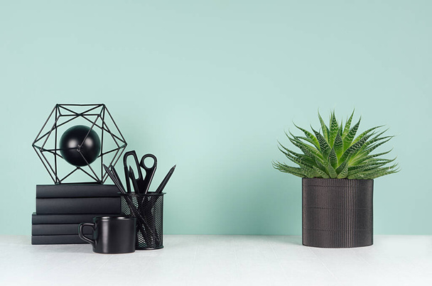 Simple minimalistic office interior with black stationery, books, coffee cup, aloe plant, abstract sculpture in green mint menthe interior on white wood table, copy space. - 写真・画像