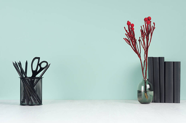 Modern elegant home workplace with black stationery, books, glass vase with red branch in green mint menthe interior on white wood table. - 写真・画像
