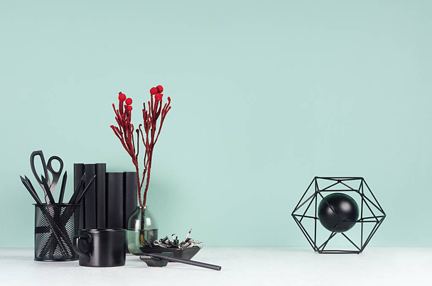 Fresh home workplace with style black stationery, books, coffee cup, abstract statuette, decorative bizarre red branch in trendy green mint menthe interior on white wood table. - Fotó, kép