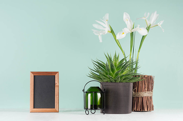 Fresh spring interior with green aloe, candlestick, decorative sheaf of brown twigs, blank photo frame, black books, white flowers on  green mint menthe wall, white wood table. - Фото, изображение