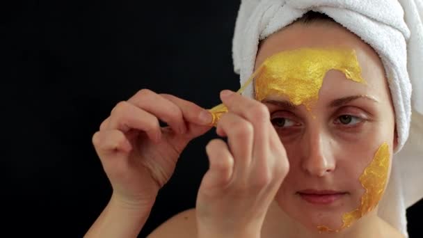 Kobieta zdejmująca złotą maskę hydrożelu na twarzy - Materiał filmowy, wideo