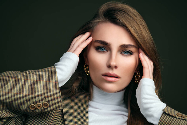 A young beautiful blonde woman in a white turtleneck and a mans jacket poses on a green olive background in the studio. - Foto, Bild