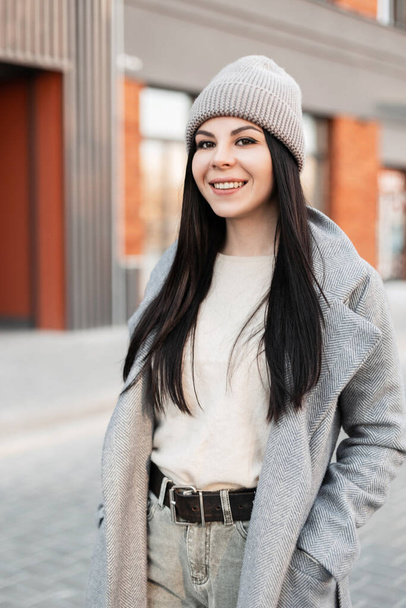 Porträt ziemlich positive junge brünette Frau in Mode Frühling Oberbekleidung mit niedlichem Lächeln posiert auf der Stadt in der Nähe moderner Gebäude. Glückliches Mädchen geht und lächelt. Trendige Kleidung für Women.Street Style - Foto, Bild