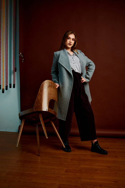 Mininalism style classic studio photo set of the young independent woman. Gorgeous young female in classic suit, black shoes and grey coat. Vintage chair. Woman's clothes. Fashionable clothes. - Photo, Image