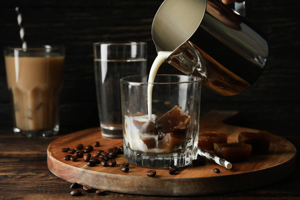 Milch wird in ein Glas Kaffee gegossen. Komposition mit Eiskaffee - Foto, Bild