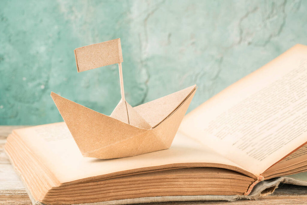 papírový člun na staré knize na stole. Ručně vyrobený origami papír plachetnice na otevřené knize - Fotografie, Obrázek