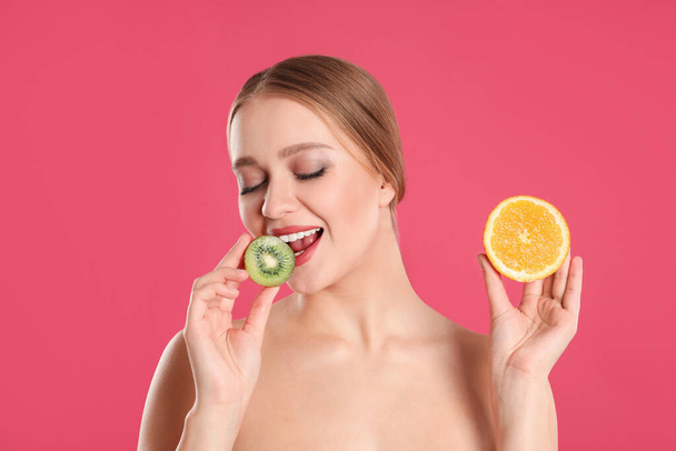 Young woman with cut kiwi and orange on pink background. Vitamin rich food - Foto, Bild