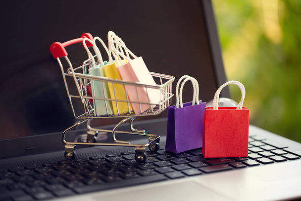 Online winkelen, e-commerce concept: Papieren boodschappentassen in een trolley of winkelwagentje op de natuurlijke groene achtergrond. aankoop van producten op internet kan kopen goederen uit het buitenland - Foto, afbeelding